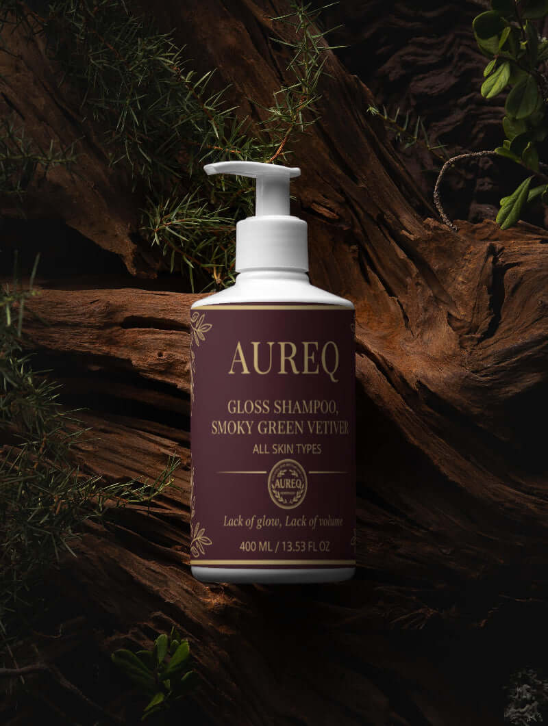 AUREQ gloss shampoo bottle on wood backdrop, promoting smooth and shiny hair for all skin types.